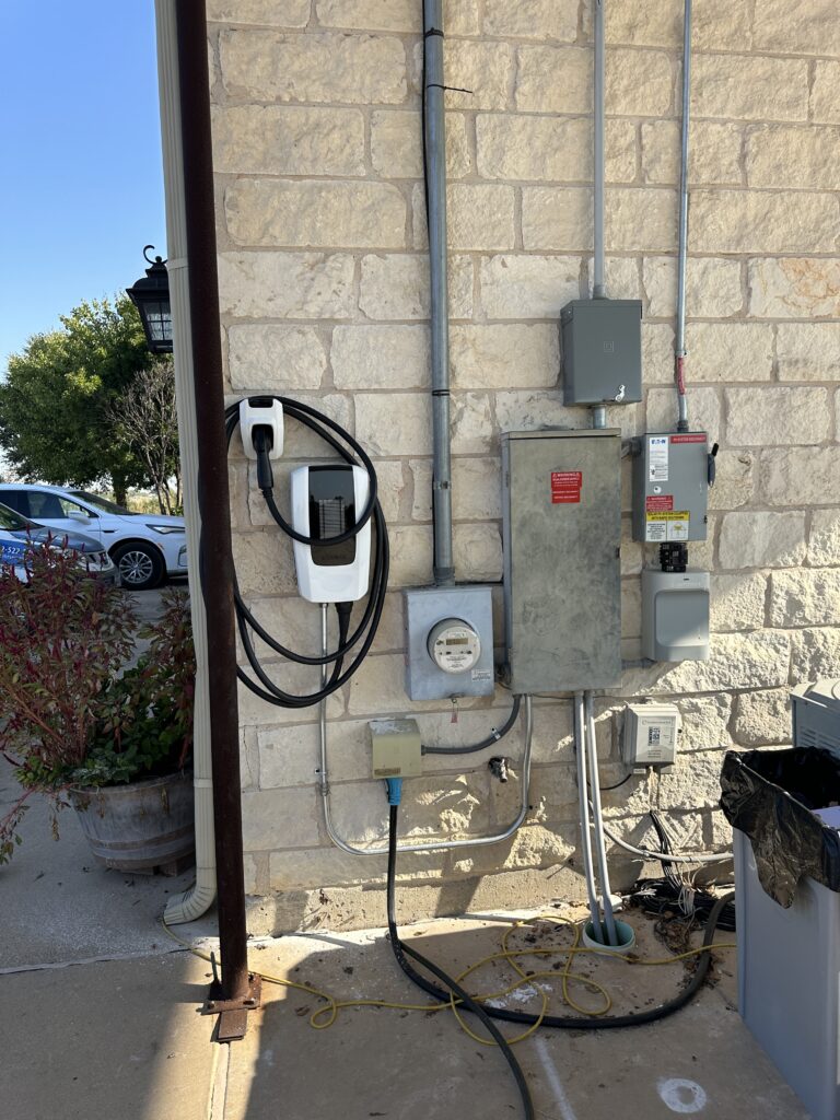 Tesla Wall Connector installed beside the electric meter and panels on a stone wall