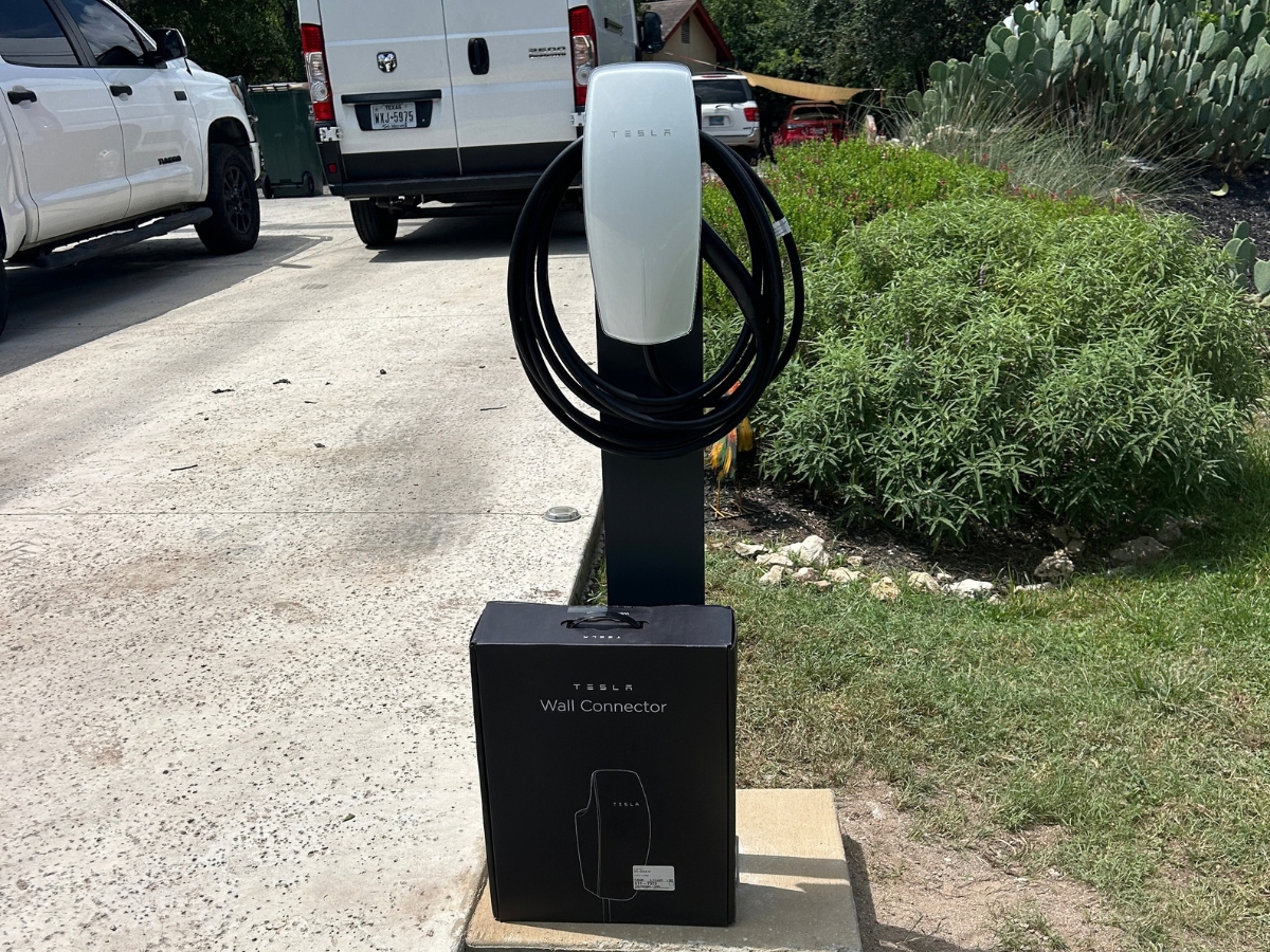 Pedestal-mounted EV charger on a poured concrete pad beside a driveway