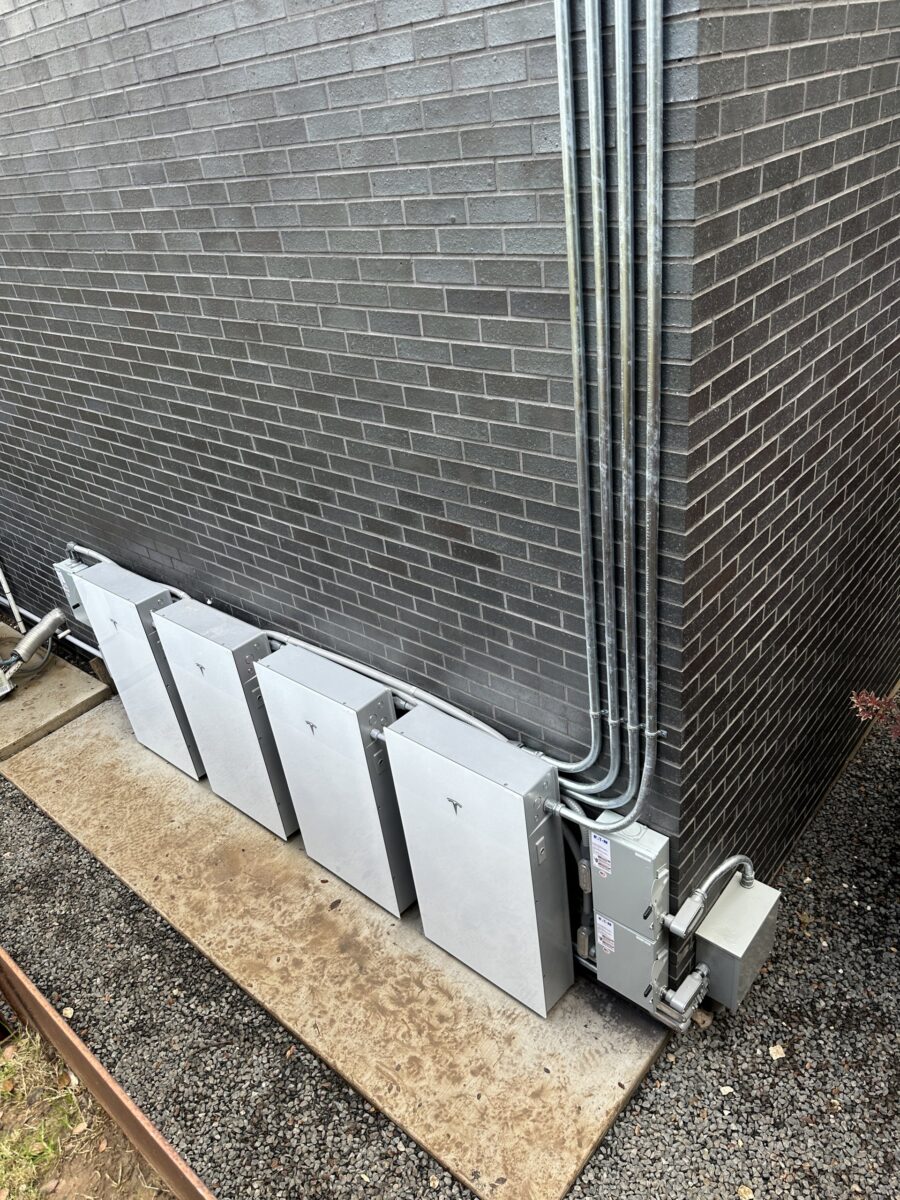 Four Tesla Powerwall 3 batteries with conduit on a dark brick wall, Westlake Hills, Texas
