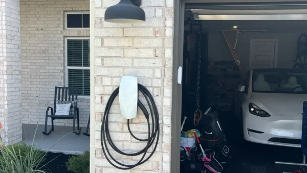 Tesla Wall Connector mounted on an exterior brick wall beside an open garage