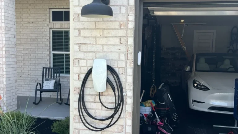 Tesla Wall Connector mounted on an exterior brick wall beside an open garage